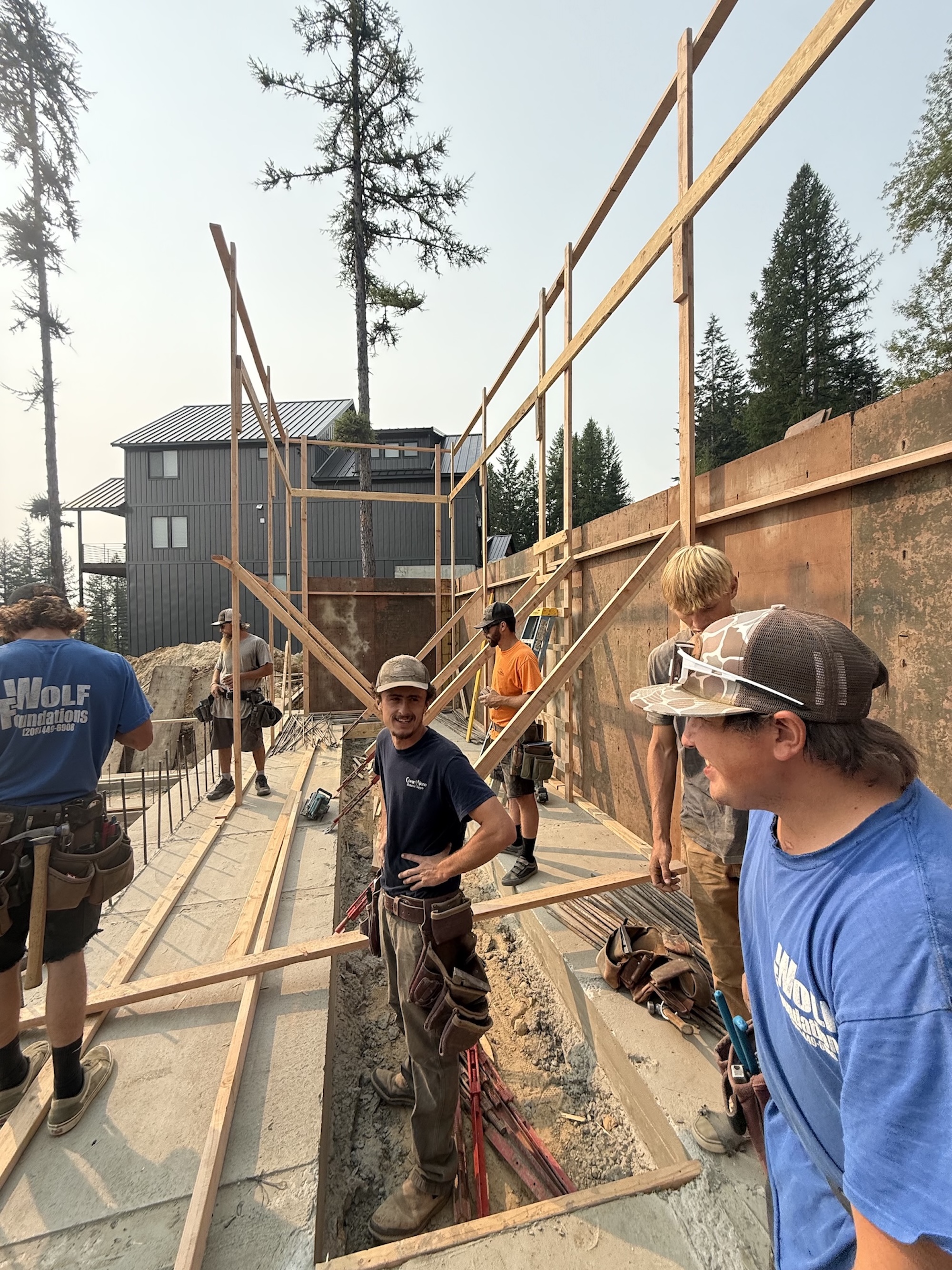 A framing crew standing on a poured foundation with wall braces going up behind them.