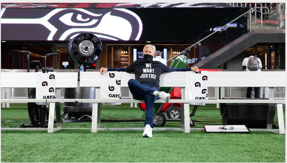 Pete Carroll on an empty stadium bench wearing a mask that reads we want justice.